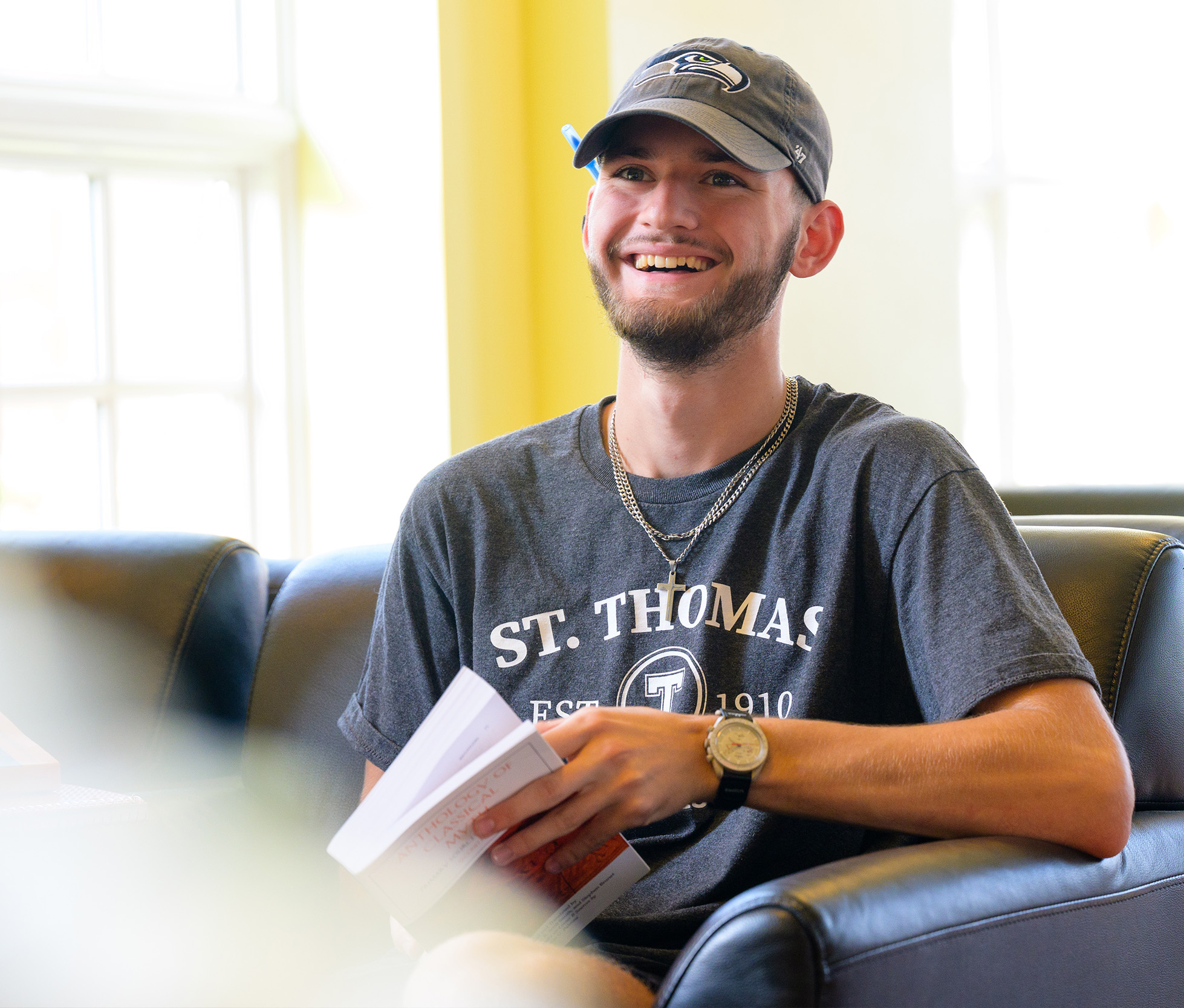 A male student in Study Hall, holding a book and smiling