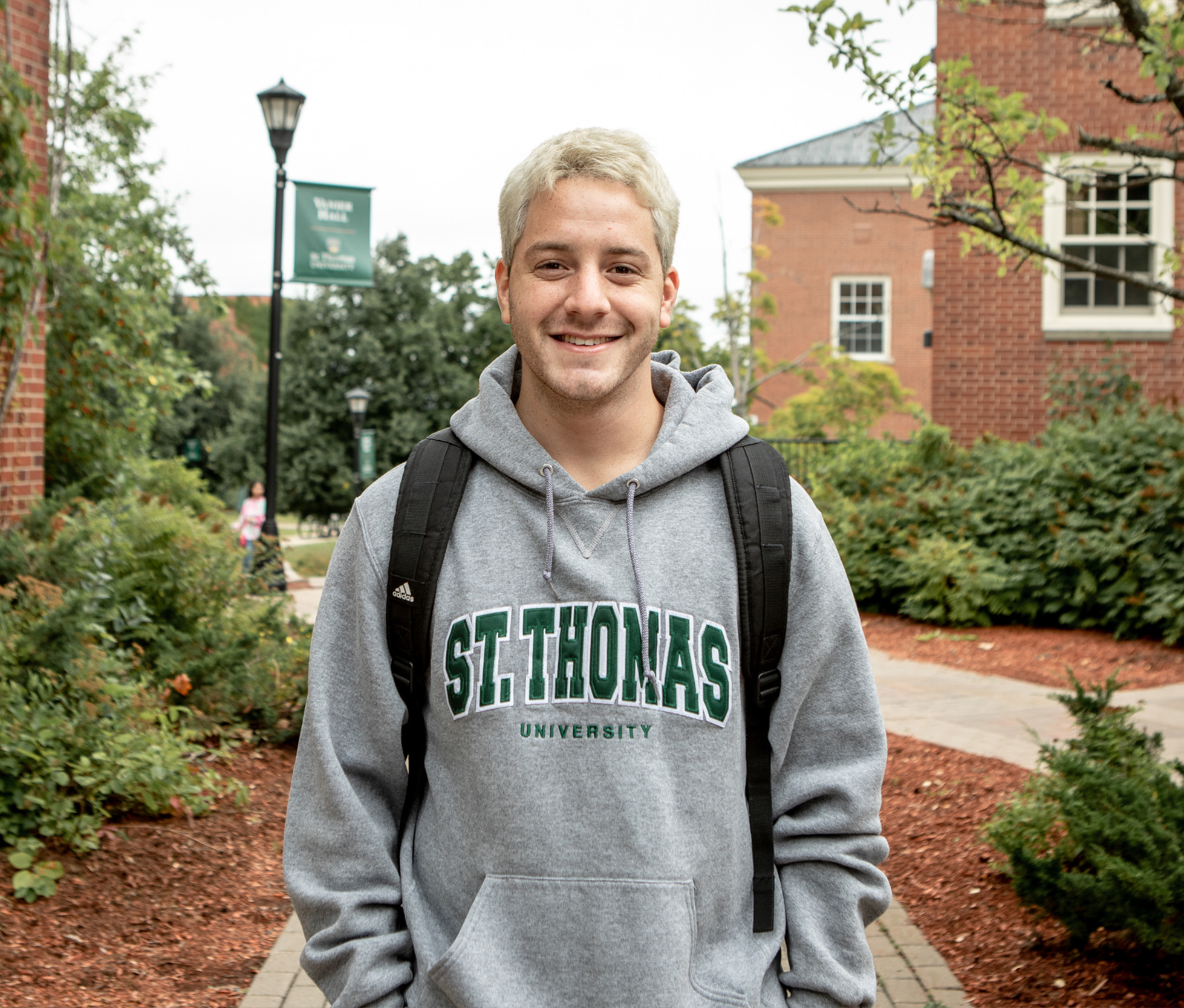 A male student wearing a St. Thomas University sweater, smiling on campus