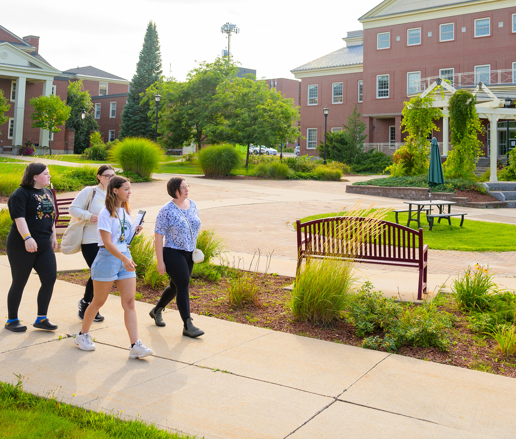 A student walking through upper campus with three individuals on a campus tour