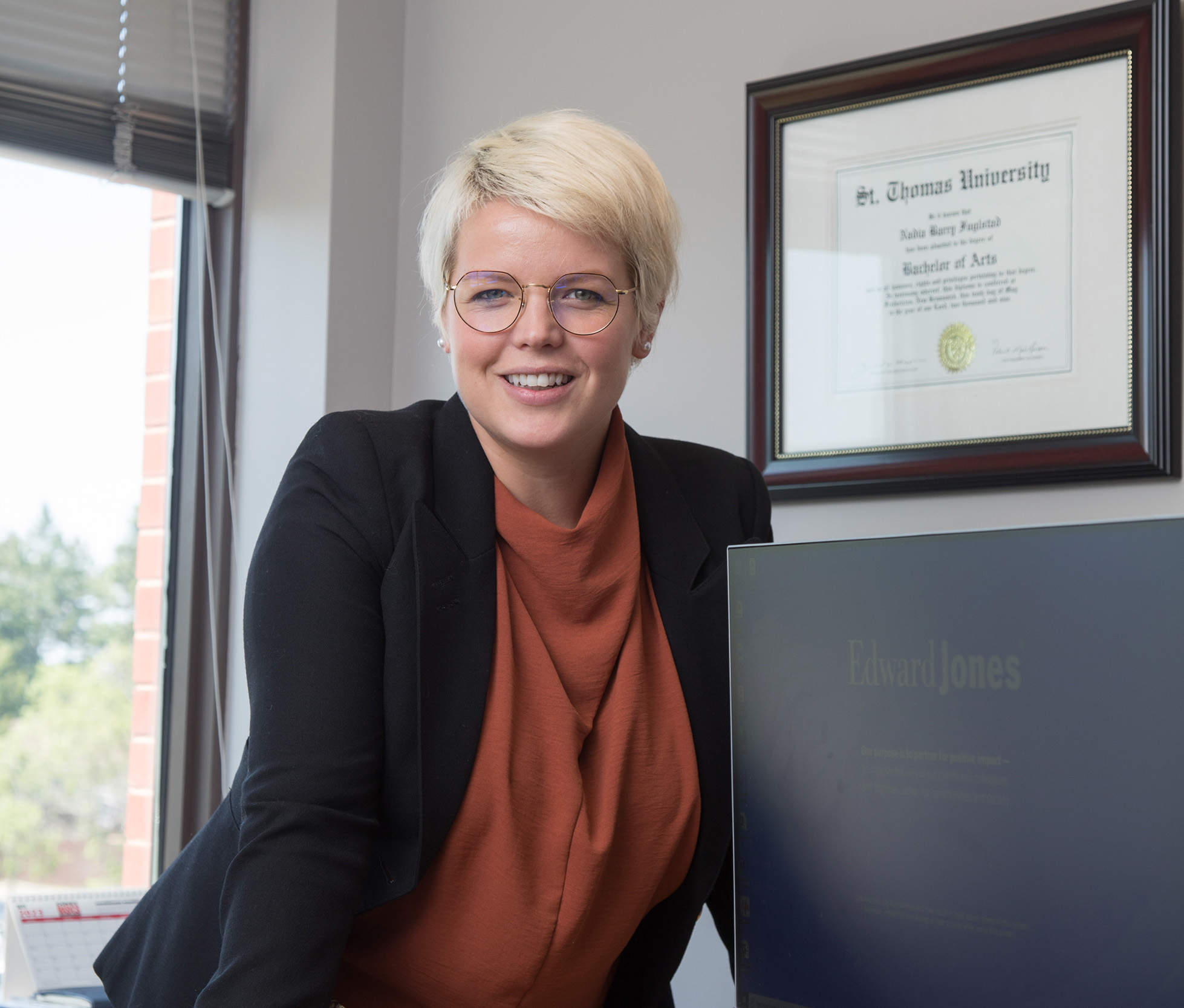 A STU alumna standing behind her desk with her St. Thomas University diploma in the background