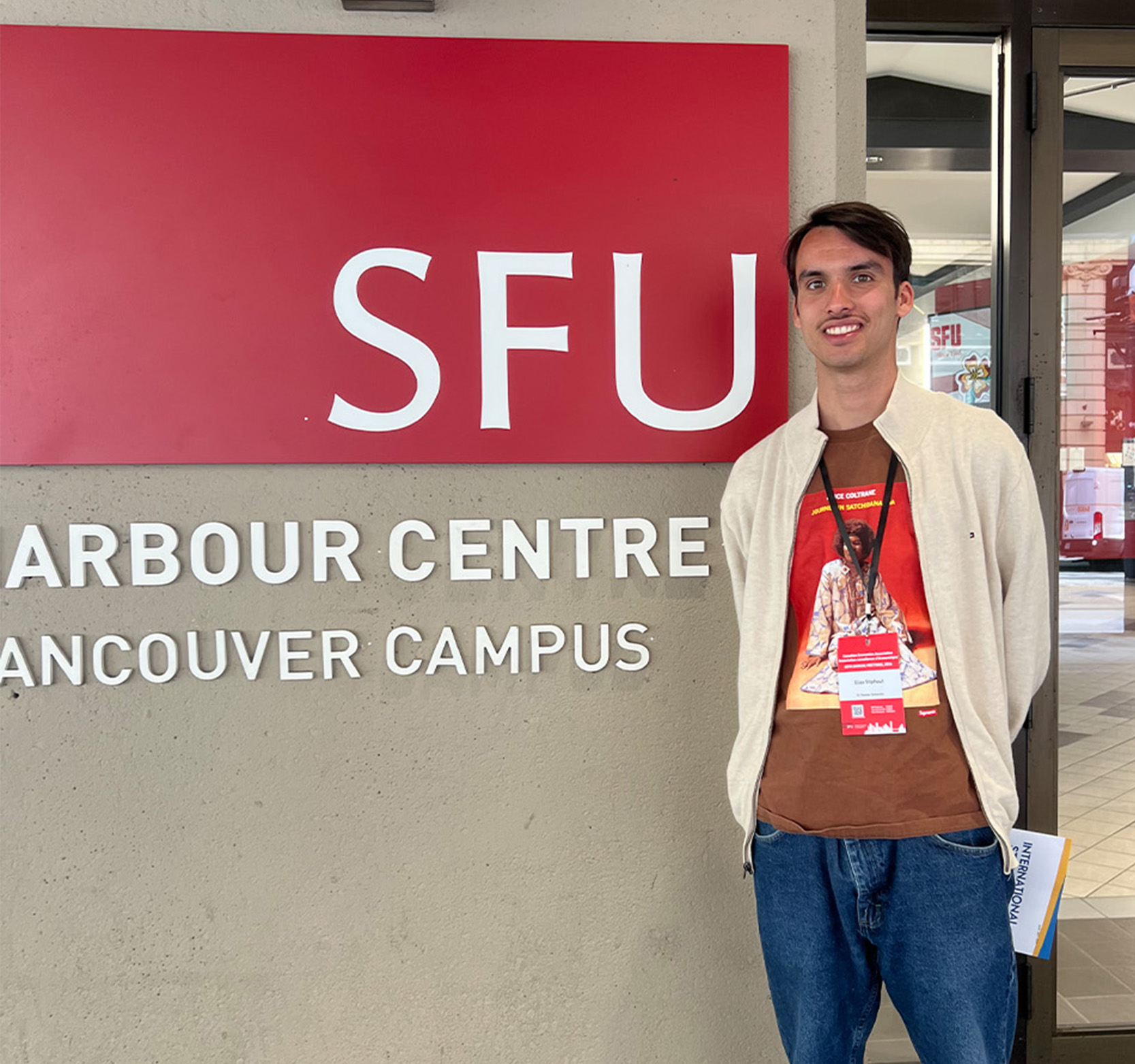 A male student stands in front of a building with the letters SFU on the outside