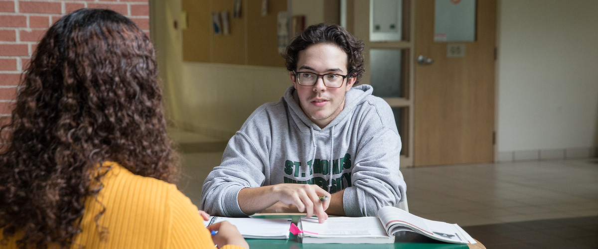 Two students at a table with an open textbook in front of them