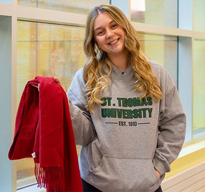 A student holding up a red scarf in front of a window on campus