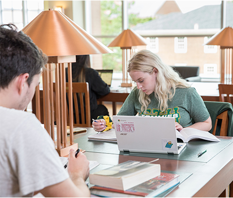 Students sitting at desks studying with laptop and books in Study Hall