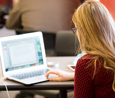 A student sitting at a table on campus using her laptop