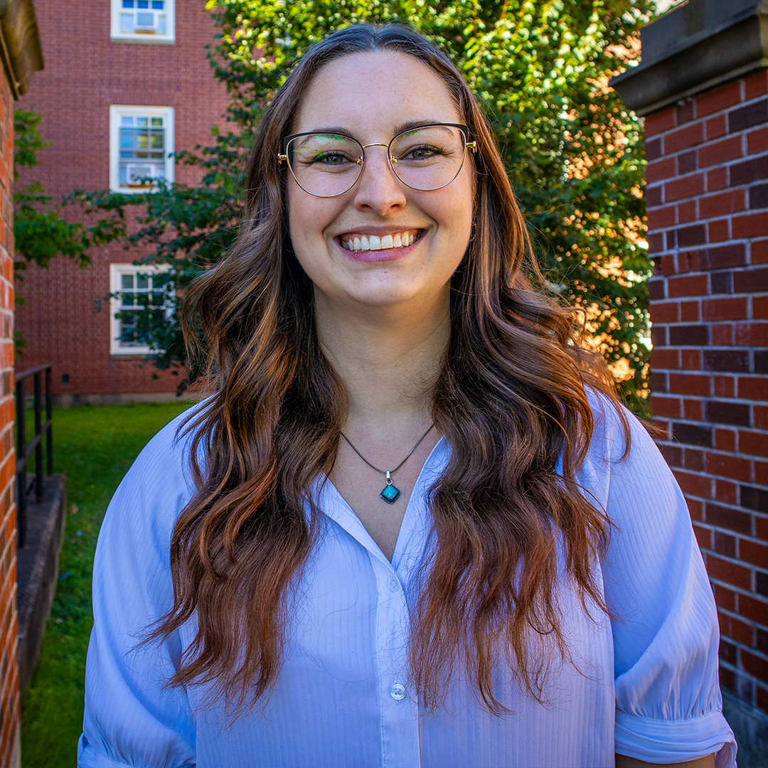 A woman standing on campus in front of a tree.
