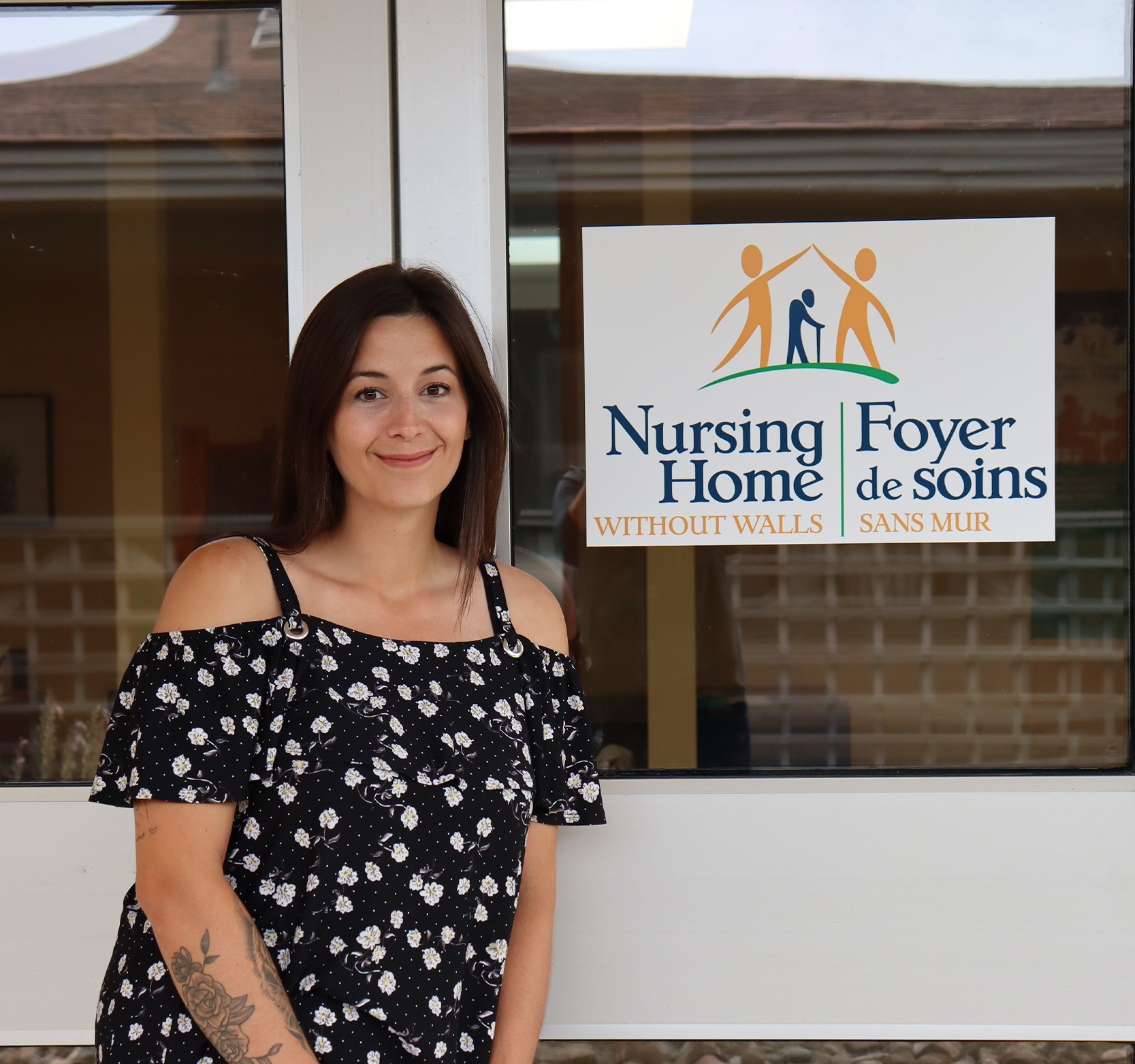 Candace standing in front of Nursing Home Without Walls logo/door