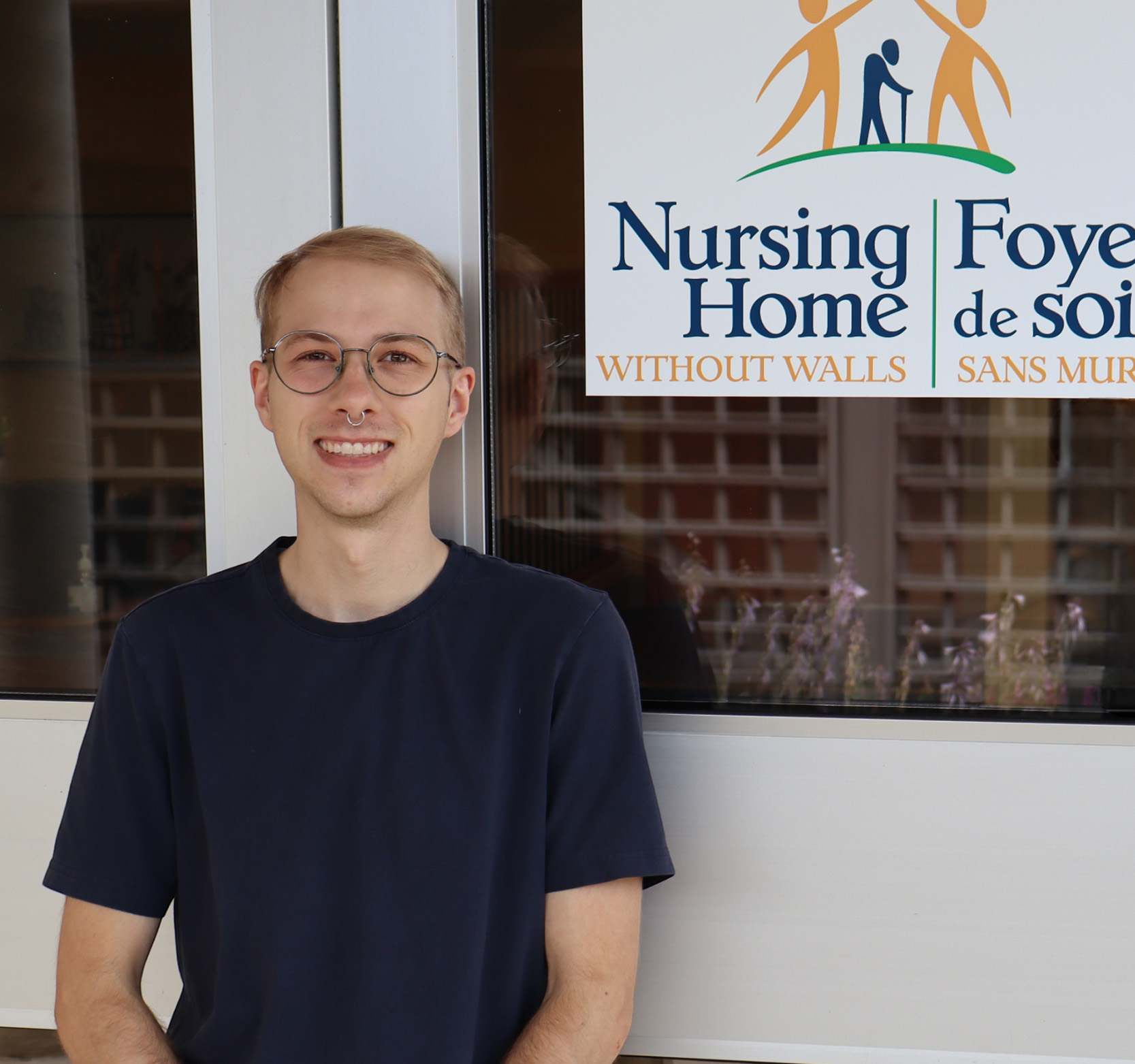 Emmett standing in front of Nursing Home Without Walls logo/door