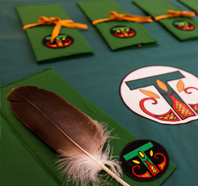 Eagle feather laid on a green table cloth with the Indigenous T logo