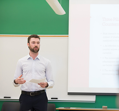 Male student standing and giving a presentation on a projector in classroom