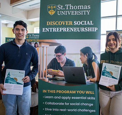 Two students holding program sheets at Open House in front of Social Entrepreneurship and Nonprofit Management banner