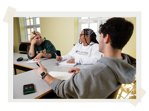 Three students sit in a classroom having a discussion