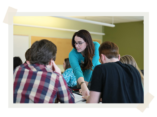 Dr. Karla O'Regan in the classroom, leaning over the table to talk to a small group of students