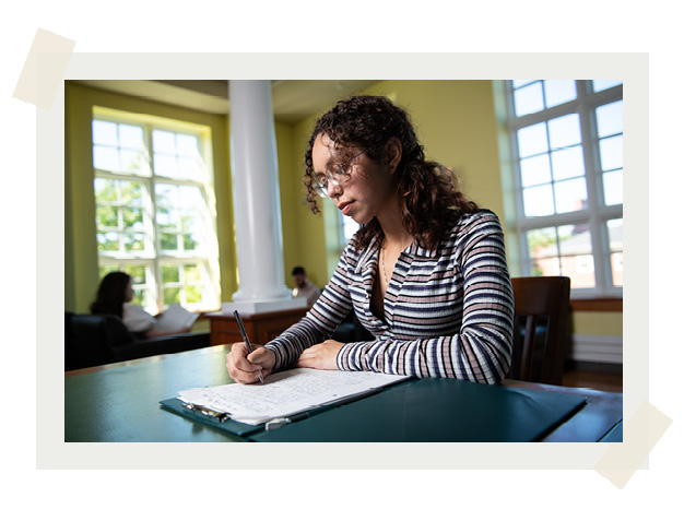 A female student sitting at a table in the study hall writing in a notebook