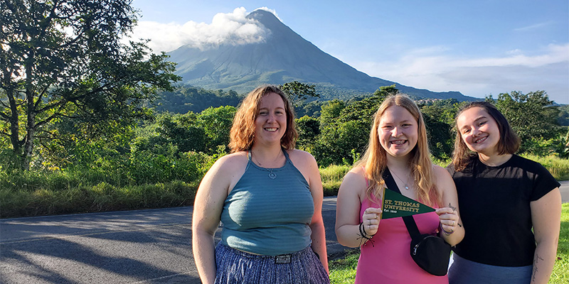 Group of 3 students smiling in nature with mountain in the background