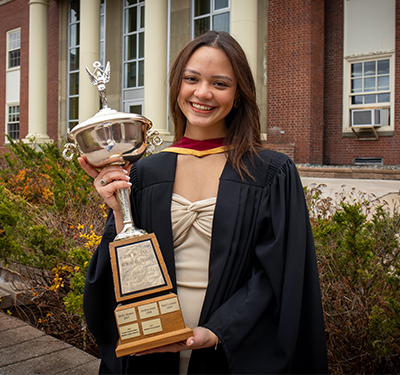 Estefania Martinez in a graduation gown holding the Thomas McCann Memorial Trophy